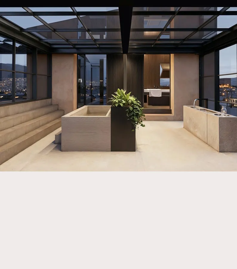Rendering of a glass-roofed bathing room with stone tub, stepped seating and a bedroom beyond, city lights outside