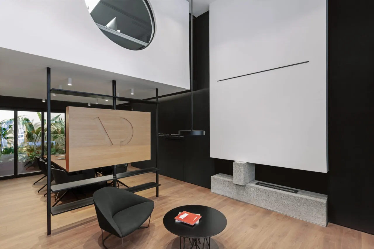 Double-height studio interior with black walls, a floating timber partition carved with the AD mark, and a concrete hearth