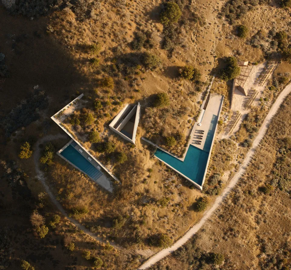 Rendering, seen from above, of a villa with V-shaped pools cut into a dry hillside beside a dirt track