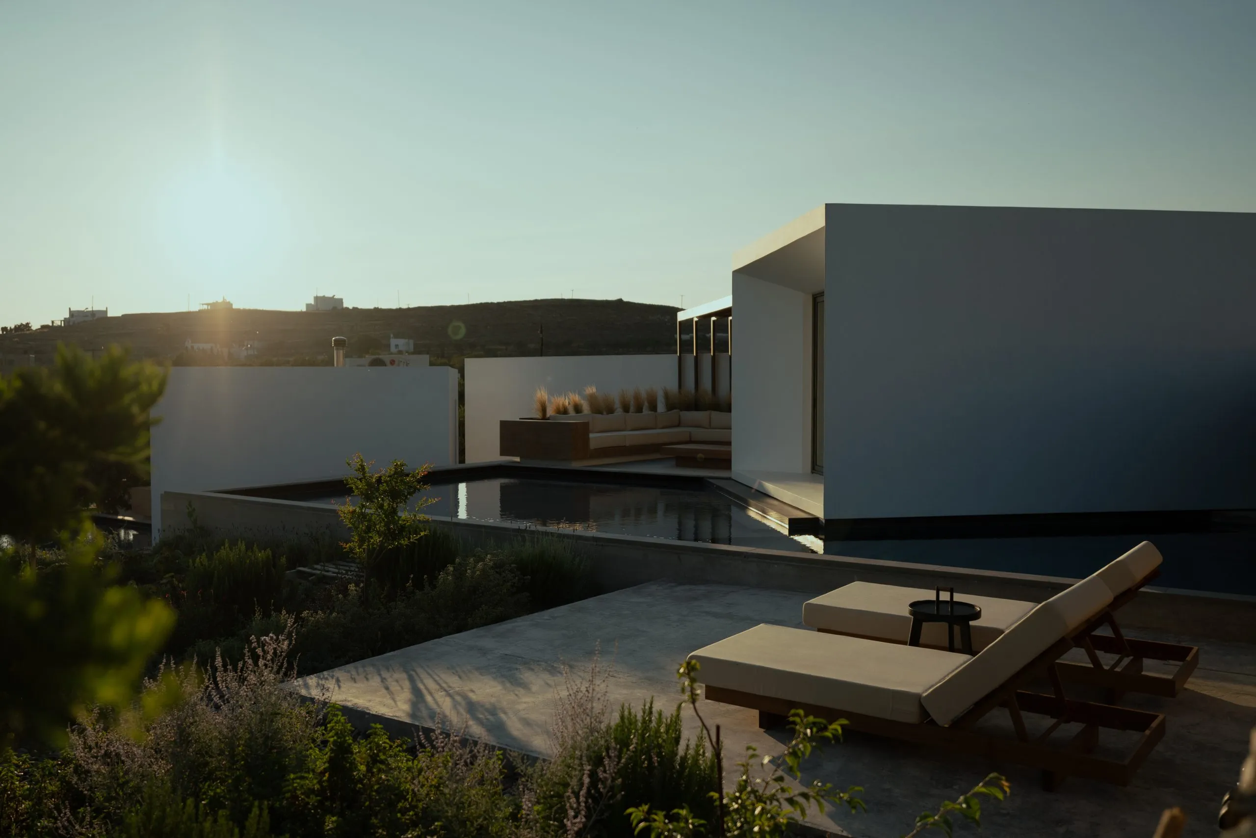 Pnoes Tinos: white cubic villa volumes around a dark pool with sun loungers at sunset