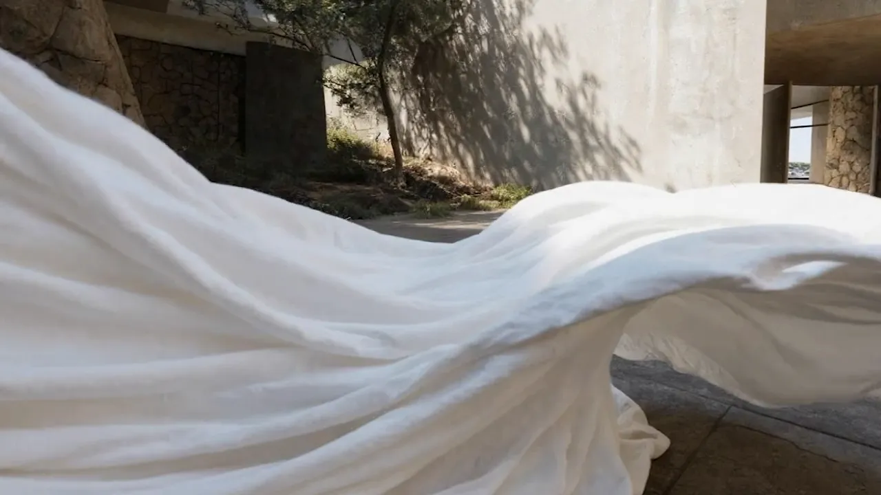 Billowing white fabric sweeping across a courtyard in front of a stone and concrete building