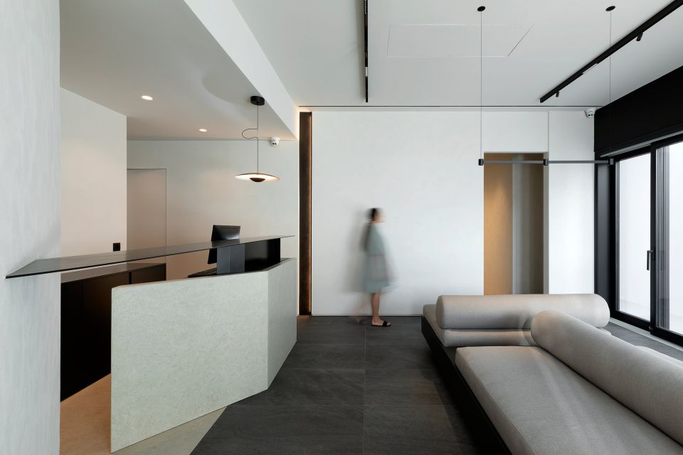 A hotel reception with a white desk and a long upholstered bench, a guest passing through