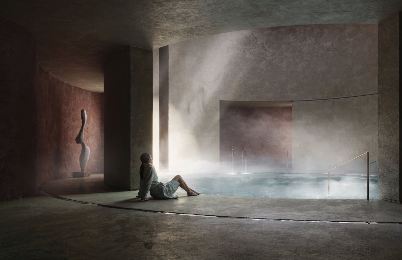 A guest resting beside a steaming indoor pool in a stone spa lit by a shaft of daylight