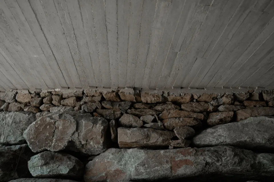 A board-marked concrete slab resting on an old rubble stone wall
