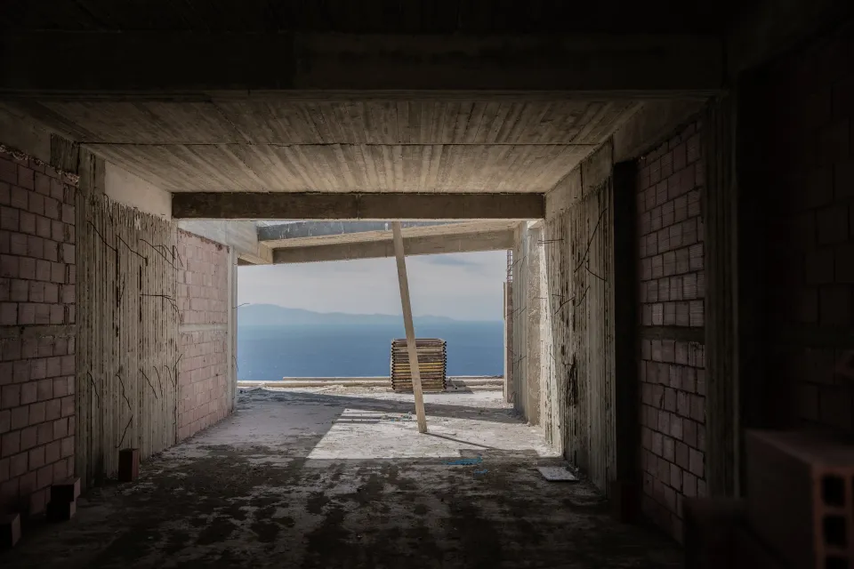 An unfinished concrete frame with brick walls, opening onto the sea