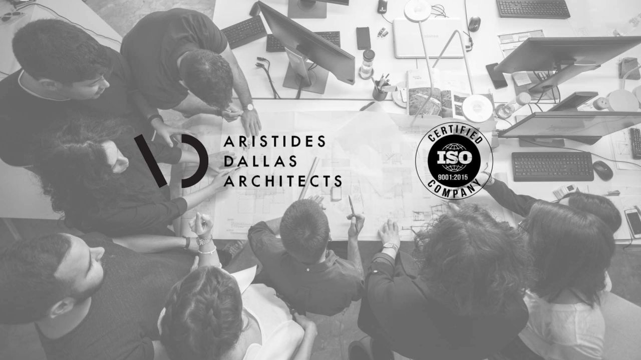 Architects gathered around drawings on a desk, overlaid with the Aristides Dallas Architects logo and an ISO 9001:2015 certified company seal