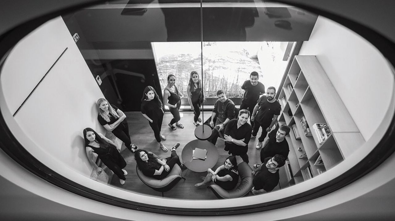 Black and white group portrait of the studio team looking up, photographed from above through an oval window beside a bookshelf