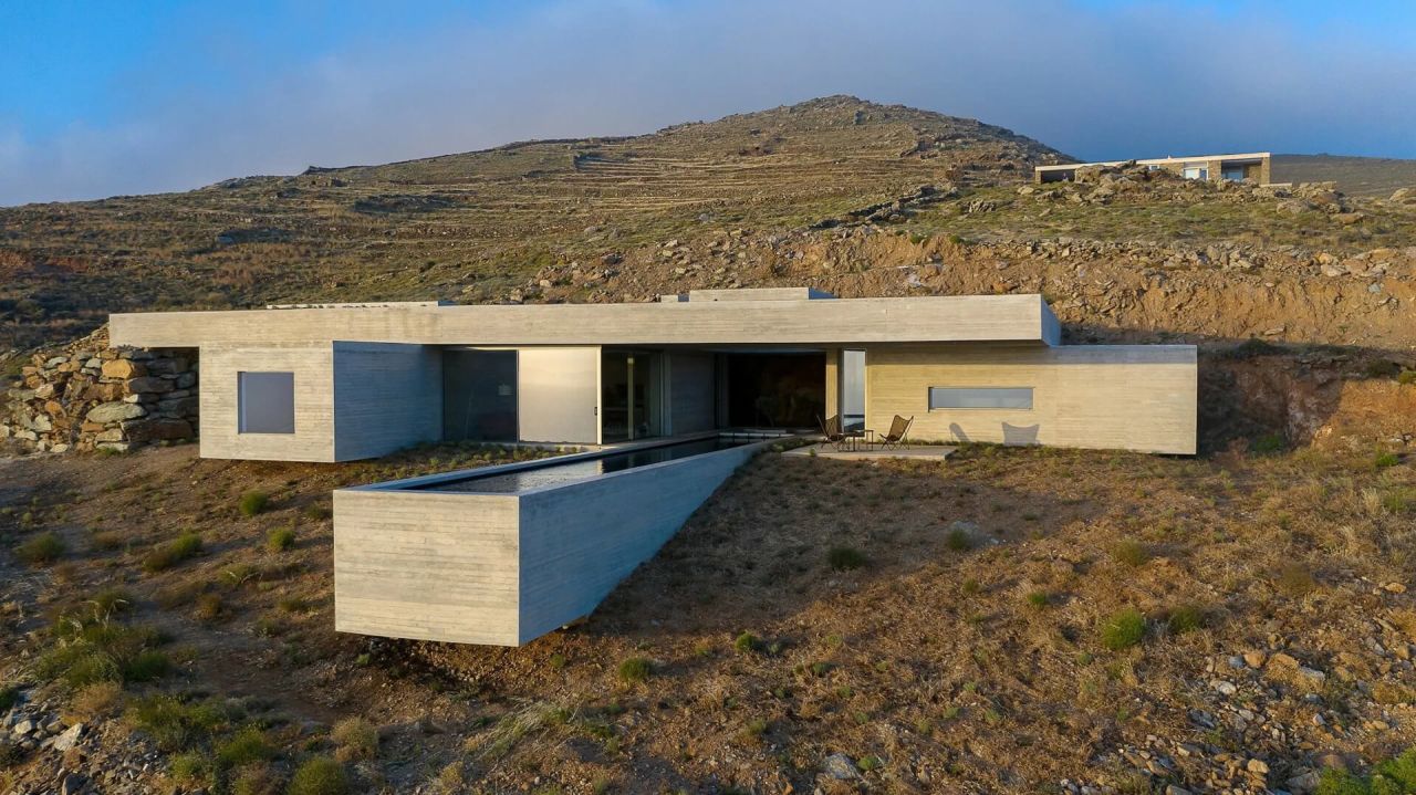 Low concrete house with a long narrow pool in front, set into a terraced mountain slope at golden hour