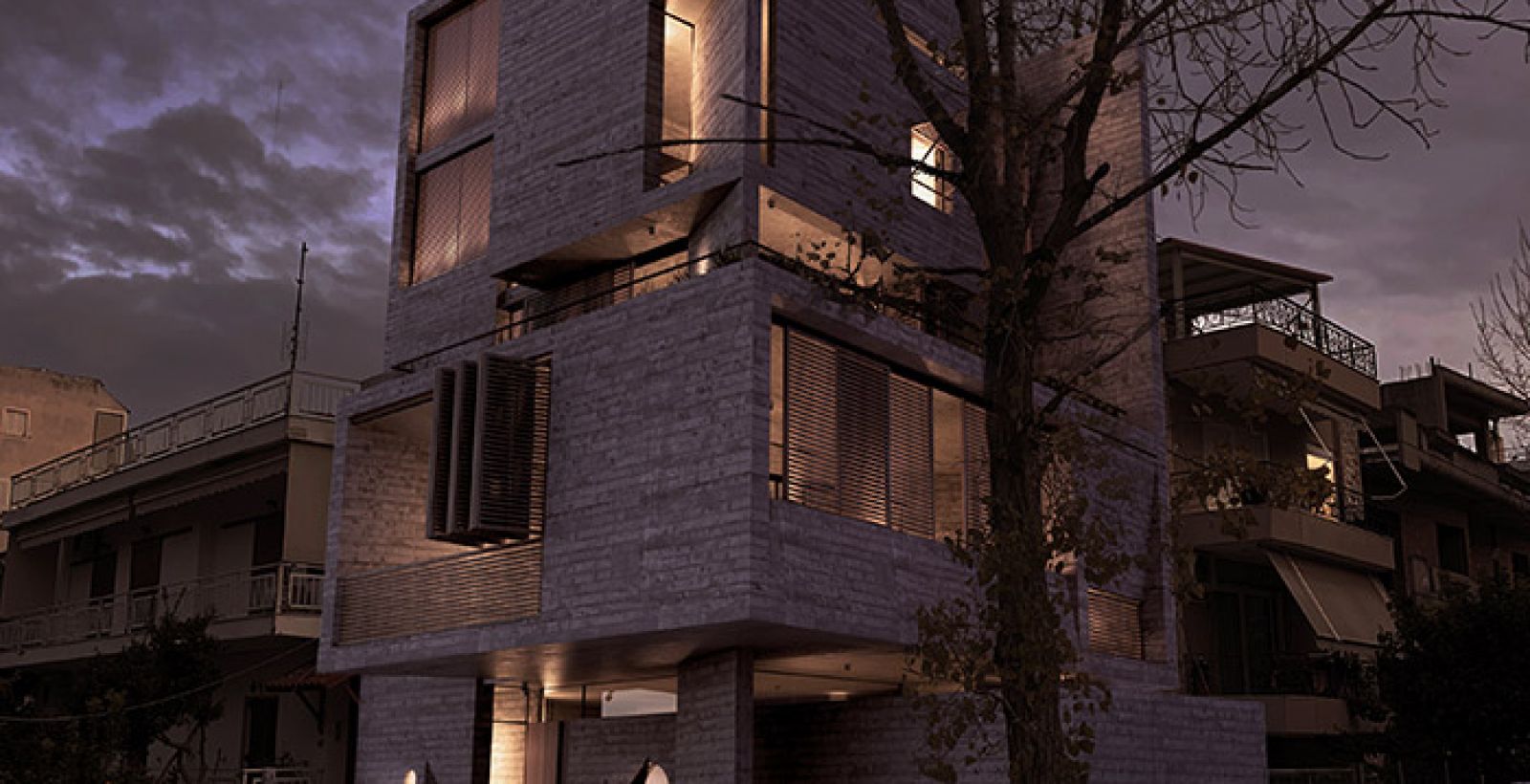 Rendering of Casa Leone at dusk on an Athens street: lit concrete apartment block behind a bare tree and parked cars