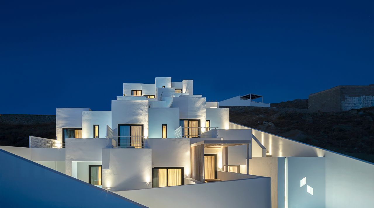 Cubic Hotel, Mykonos: stepped white cubic volumes glowing with warm light against a deep blue night sky