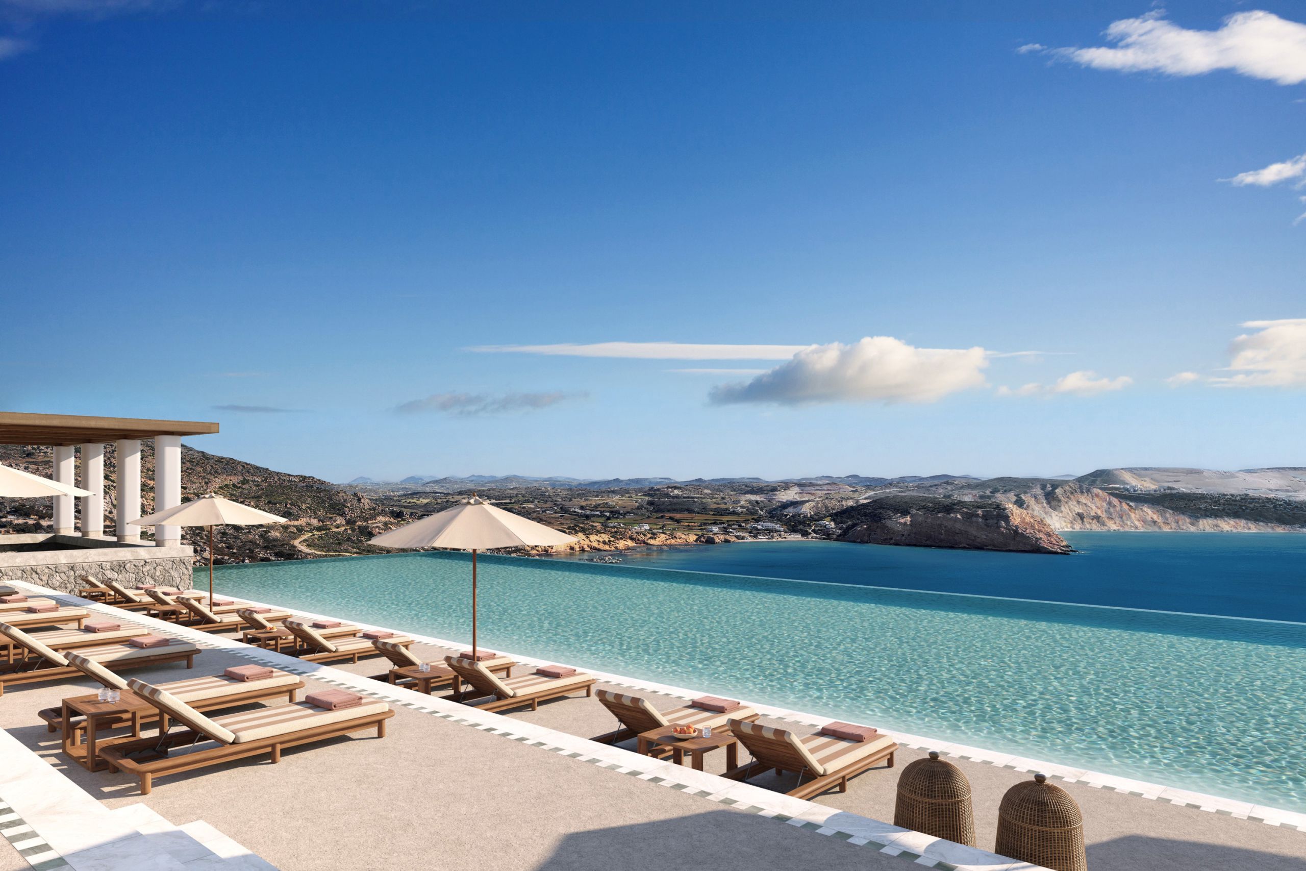 Infinity pool lined with wooden sun loungers and parasols, overlooking the bay and the hills of Milos