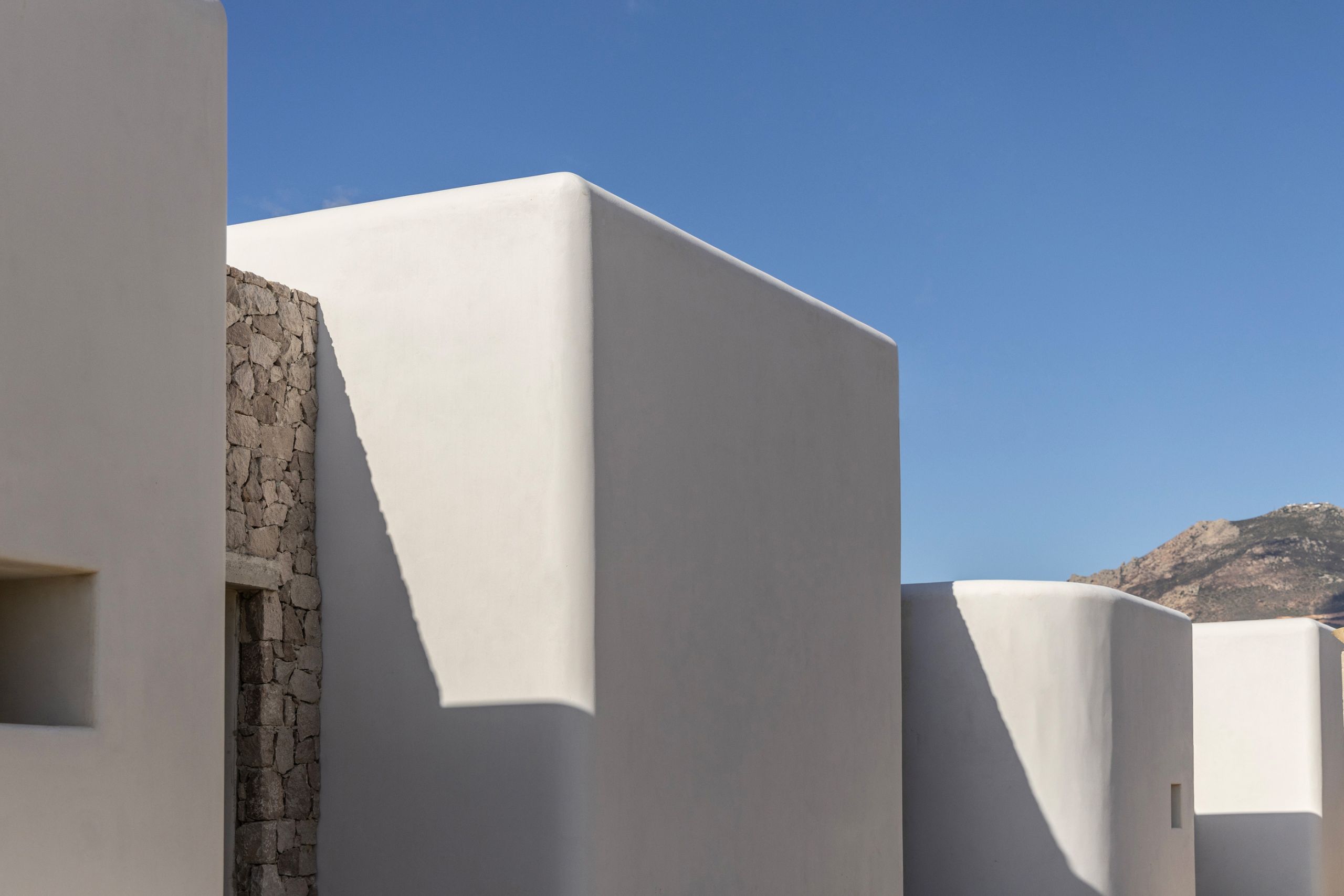 White plastered volumes with rounded edges and a stone wall against a deep blue sky
