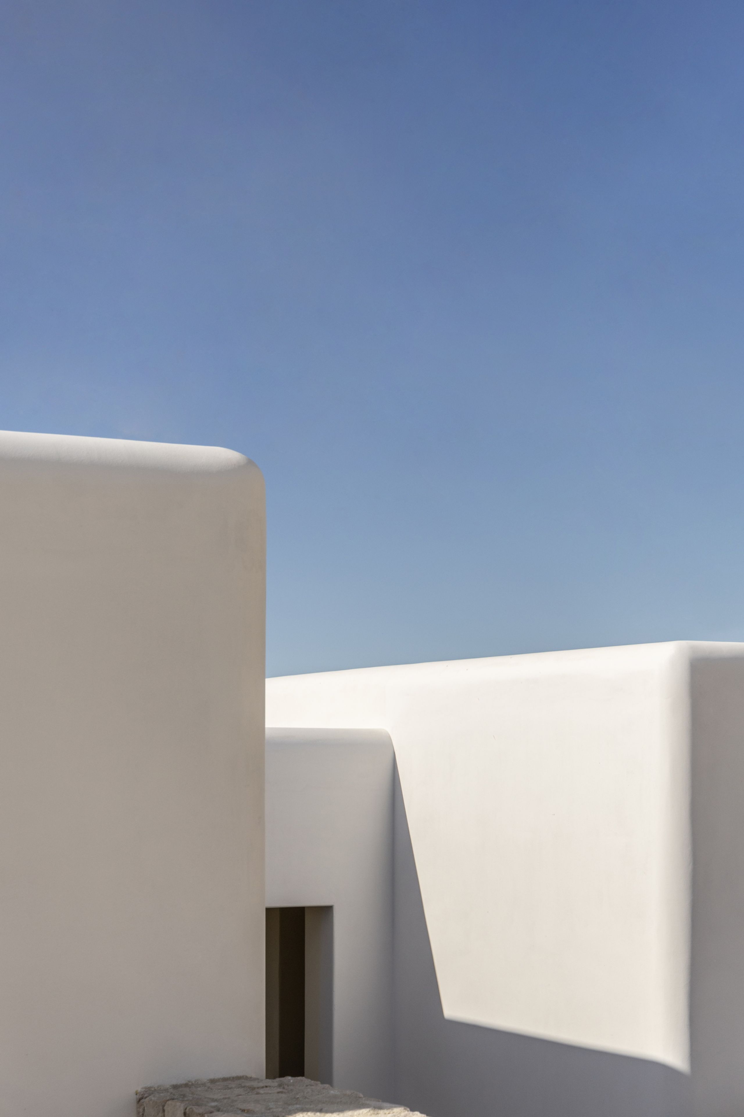 White plastered volumes meeting at rounded corners under a blue sky