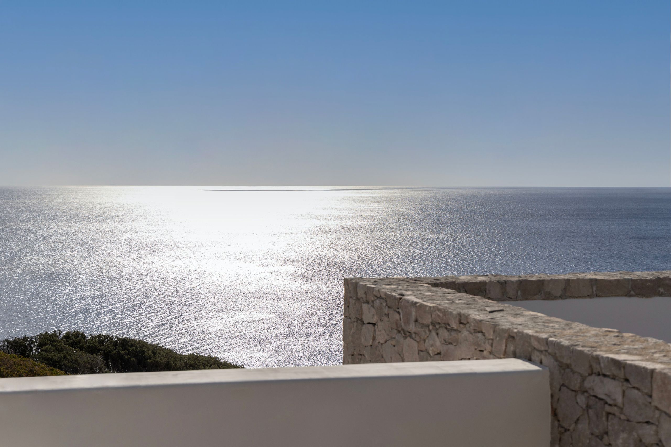 Sunlight glittering on the sea beyond a white parapet and a stone wall