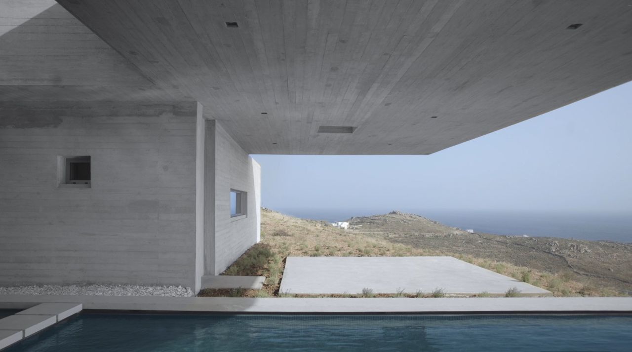 The Lap Pool House: a board-marked concrete canopy frames the hills and the sea beyond a long pool and stone terrace