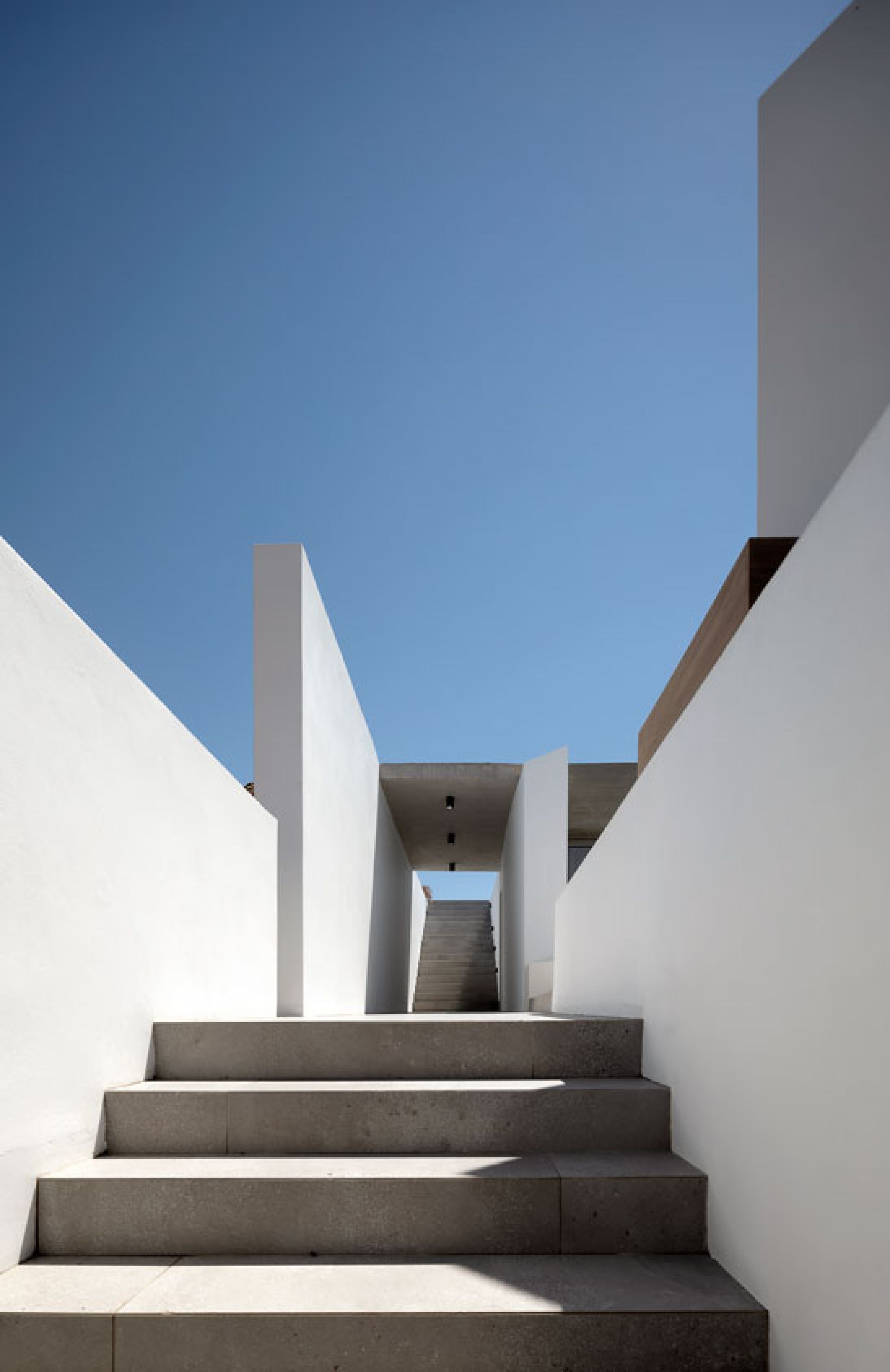 Pnoes Tinos interior: walnut door opening onto a lounge with an armchair and framed prints, beside a sculpture on a plinth