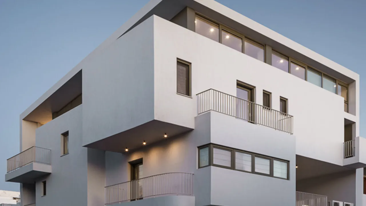 Urbanity in Tinos: cubic upper volumes with balconies and strip windows against a pale evening sky